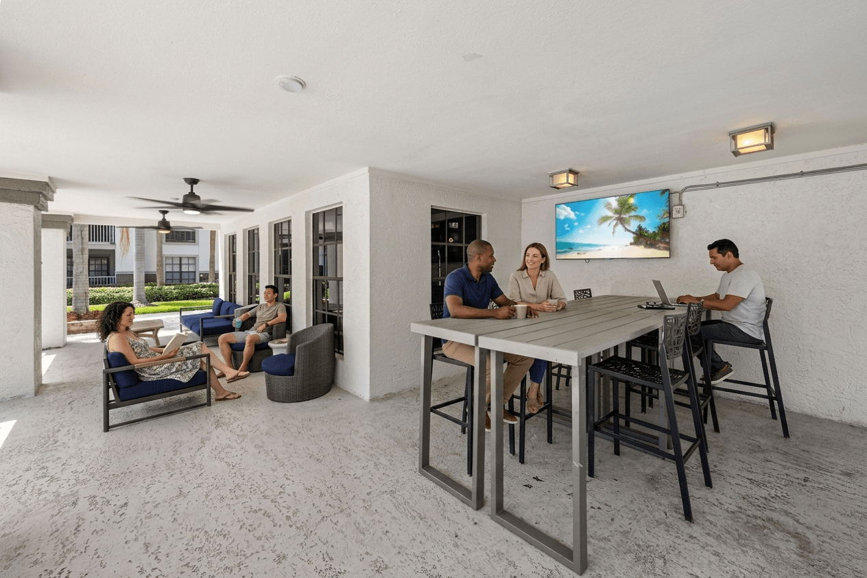 A group of people are sitting around a table in a room with a television.